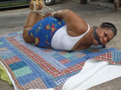 Mature ebony plumper is hogtied on a comforter while cleave gagged