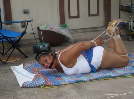 Mature ebony plumper is hogtied on a comforter while cleave gagged