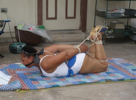 Mature ebony plumper is hogtied on a comforter while cleave gagged