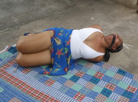 Mature ebony plumper is hogtied on a comforter while cleave gagged