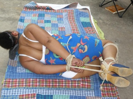 Mature ebony plumper is hogtied on a comforter while cleave gagged