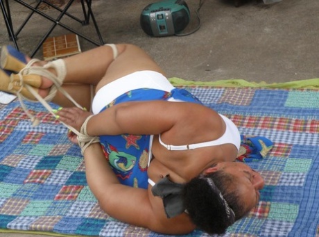 Mature ebony plumper is hogtied on a comforter while cleave gagged