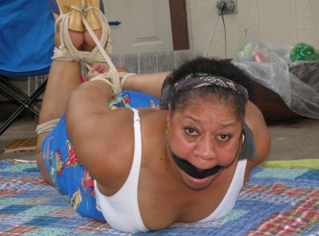 Mature ebony plumper is hogtied on a comforter while cleave gagged