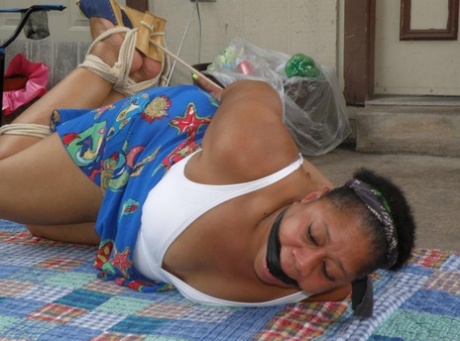 Mature ebony plumper is hogtied on a comforter while cleave gagged